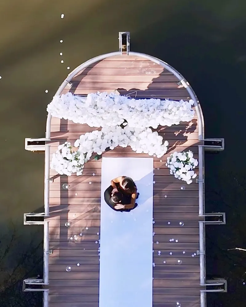 Drone view of a couple on a dock decorated with white flowers over a lake